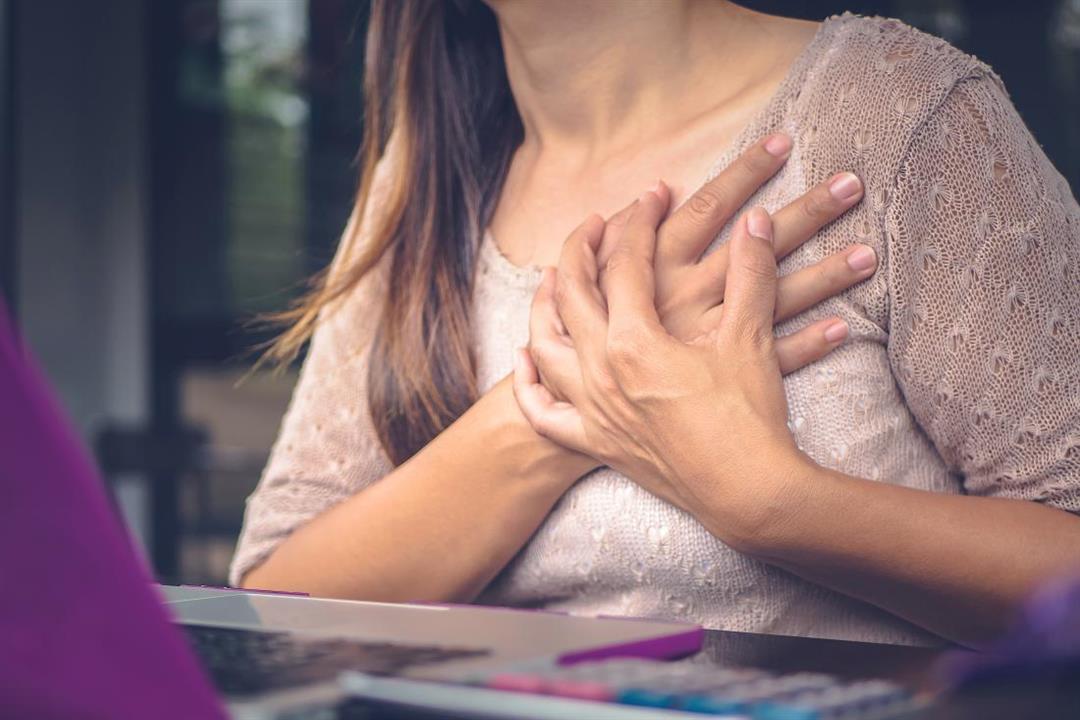 woman-with-chest-pains-clutching-her-chest-while-sitting-at-desk