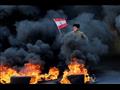 فتى يحمل العلم اللبناني وسط الدخان الأسود المنبعث 