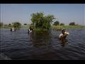 عائلة جنوب سودانية تتنقل عبر مياه الفيضانات لشراء سلع في  بينتيو على أرض مرتفعة. رحلة عودتهم تقطع حوالي 24 كيلومترًا (14.9 ميلاً)