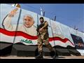  عنصر من القوات العراقية يمر أمام جدارية عليها صور