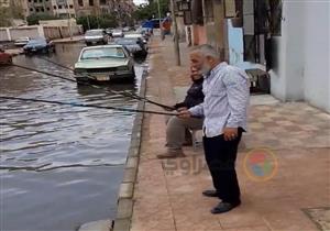 بالفيديو والصور - مواطنون يتغلبون على الظروف بالفكاهة.. يصطادون بـ"سنارة" في شوارع بورسعيد