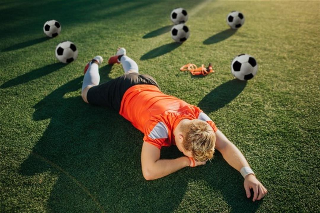 jovem-jogador-cansado-deitado-no-gramado-com-o-rosto-voltado-para-o-chao_152404-10869