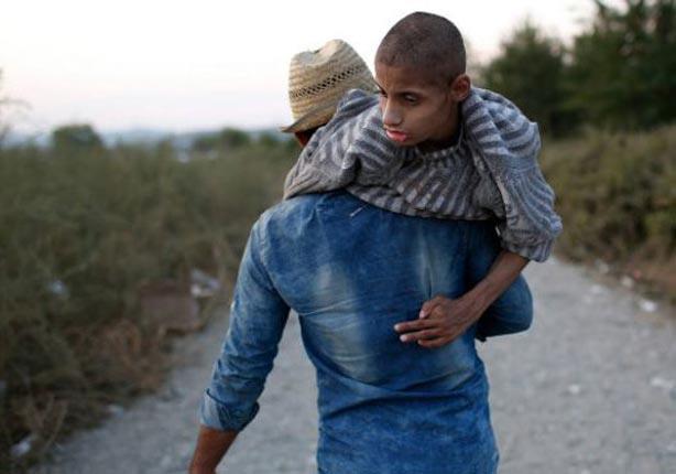 سوري يحمل شقيقه المصاب بشلل دماغي بعد عبور عائلته 