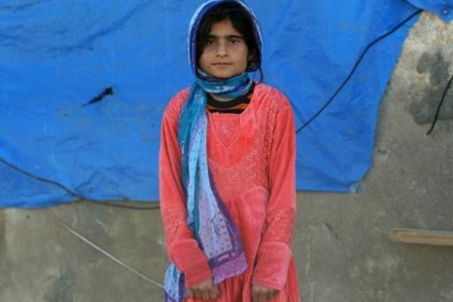 فتاة عراقية من طائفة الشبك تقف قرب منزلها الذي دمر