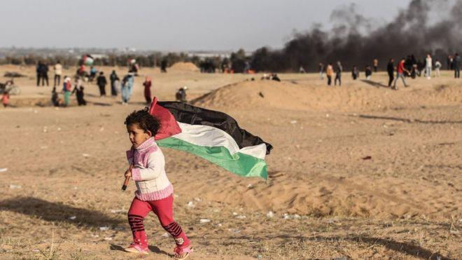 طفل فلسطينية ترفع العلم الفلسطيني قرب الحدود بين إ