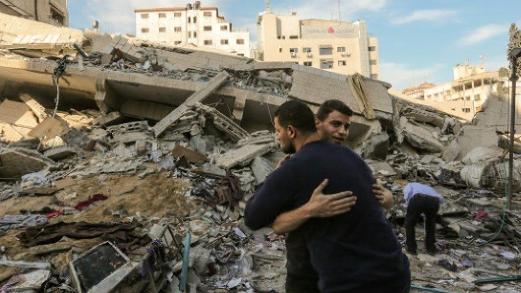 فلسطينيان يتعانقان أمام أنقاض مبنى دمر في غارة اسر