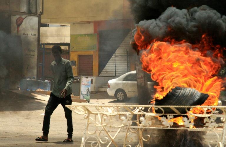 متظاهر سوداني يمر من أمام إطار مشتعل قرب مقر القيا