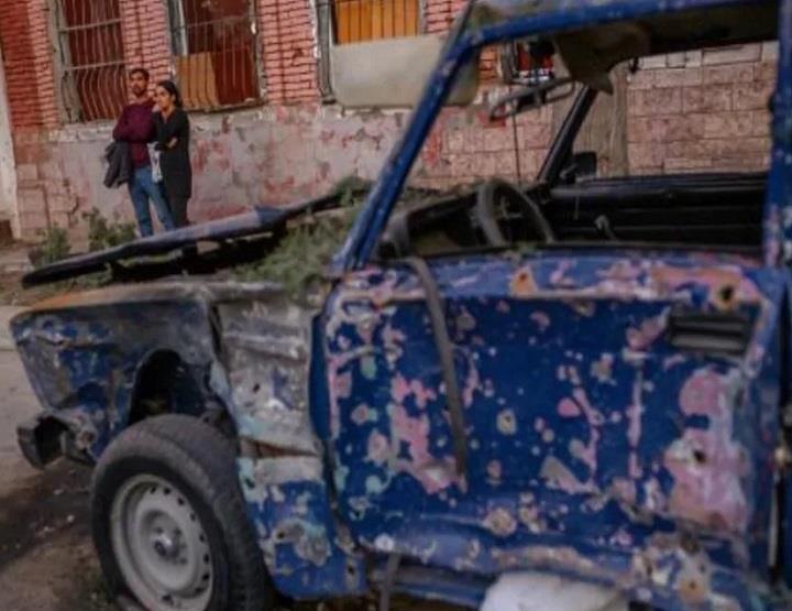  سكان محليون قرب سيارة مدمرة بعد سقوط صاروخ في شار