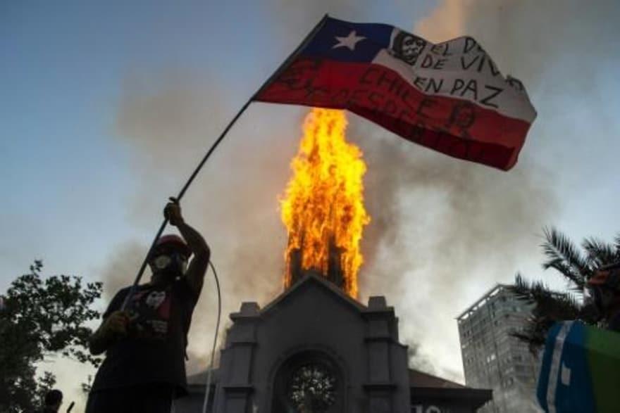 متظاهر يلوح بعلم تشيلي أمام كنيسة الصعود التي تحتر