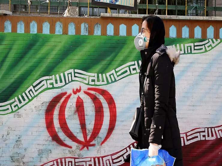 امرأة إيرانية تضع كمامة تسير قرب جدارية لعلم بلاده
