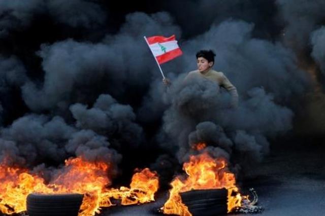 فتى يحمل العلم اللبناني وسط الدخان الأسود المنبعث 