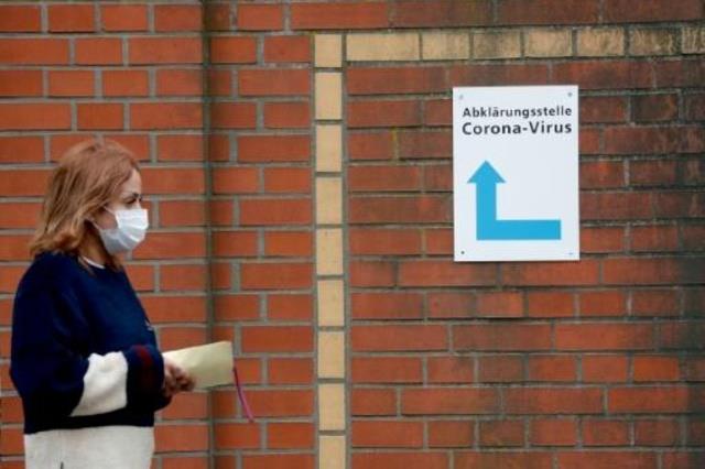 امرأة ترتدي قناعاً تعبر أمام لافتة لمركز إجراء فحو