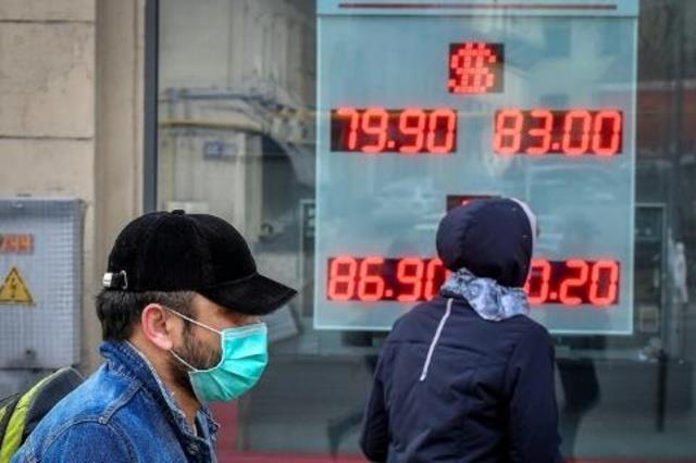 أشخاص يسيرون أمام لوح لأسعار العملات في موسكو