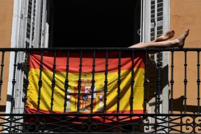 امرأة على شرفة منزلها وأمامها العلم الإسباني في مد