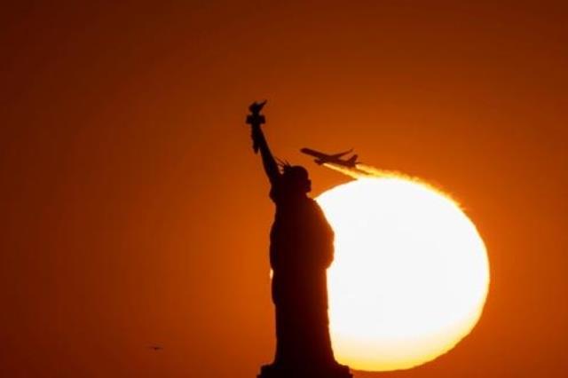 طائرة تحلق خلف تمثال الحرية عند الغروب في نيويورك 