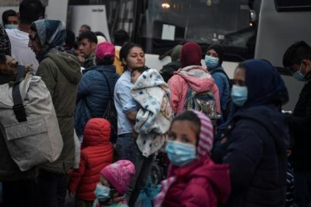 امرأة تحمل طفلاً فيما تقف بين مجموعة مهاجرين عند م