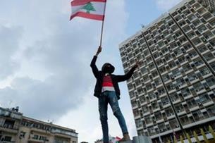 متظاهر يرفع العلم اللبناني خلال تظاهرة قبالة مؤسسة