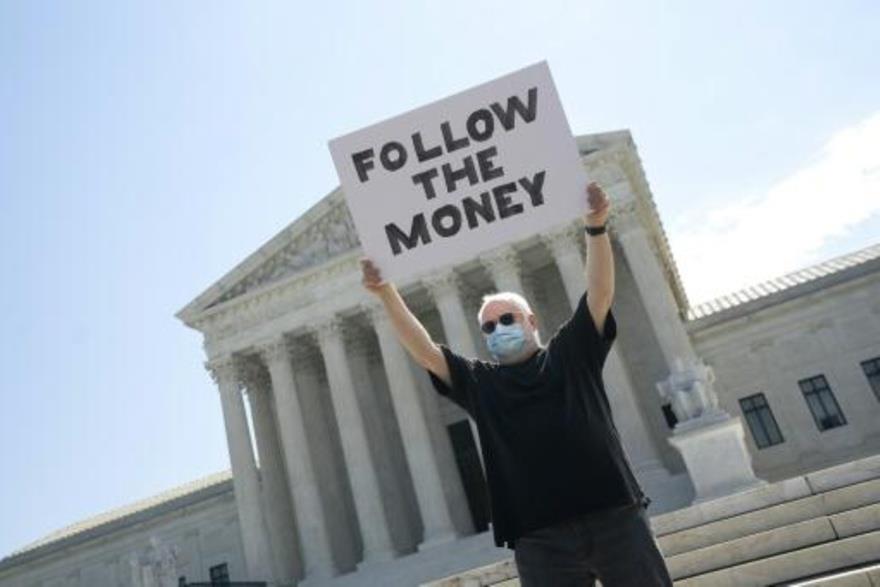 متظاهر يرفع لافتة كتب عليها تتبّعوا المال أمام مقر