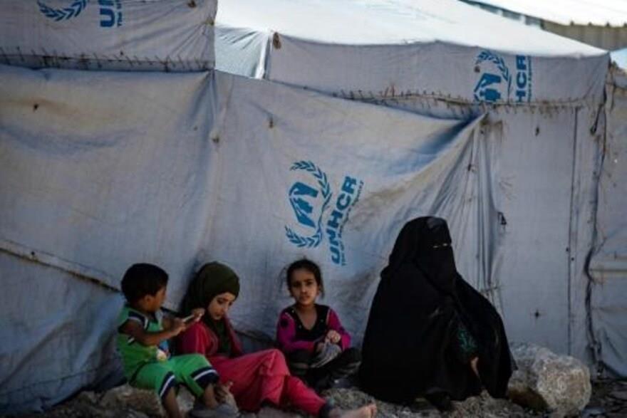 ثلاثة أطفال يجلسون مع والدتهم قرب خيمة في مخيم اله
