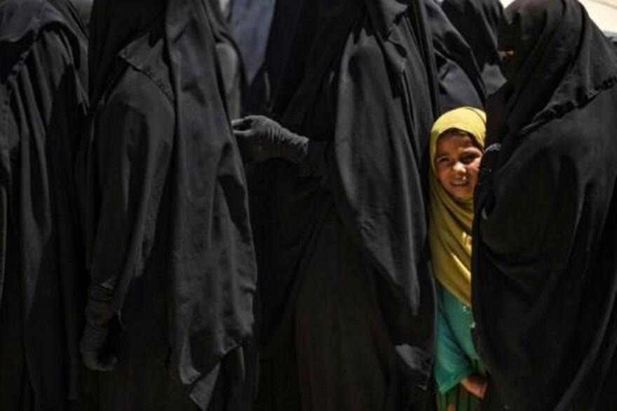 طفلة تنتظر مع نساء لتلقي مساعدات في مخيم الهول حيث