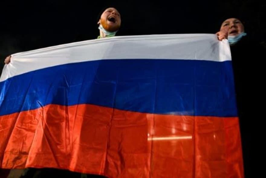  متظاهران يحملان العلم الروسي خلال الاحتجاج على قر