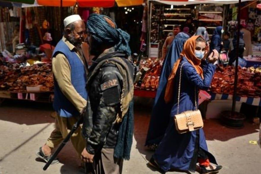 مقاتل من طالبان (وسط) يمر قرب متسوقين في سوق منداو