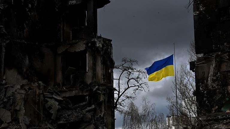 علم أوكراني بين أبنية متضررة في مدينة بوروديانكا ق