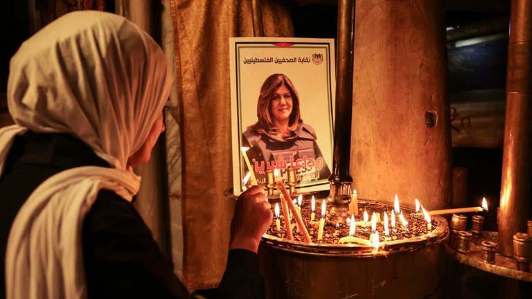 سيدة تضيء شمعة أمام صورة للصحافية شيرين ابو عاقلة 